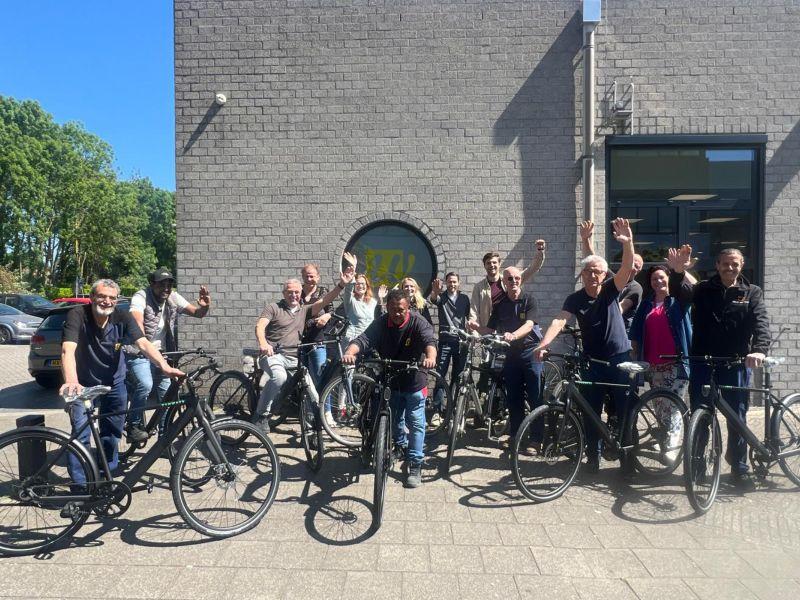 Een groep UW'ers voor het gebouw met de fiets in de hand zwaait naar de camera